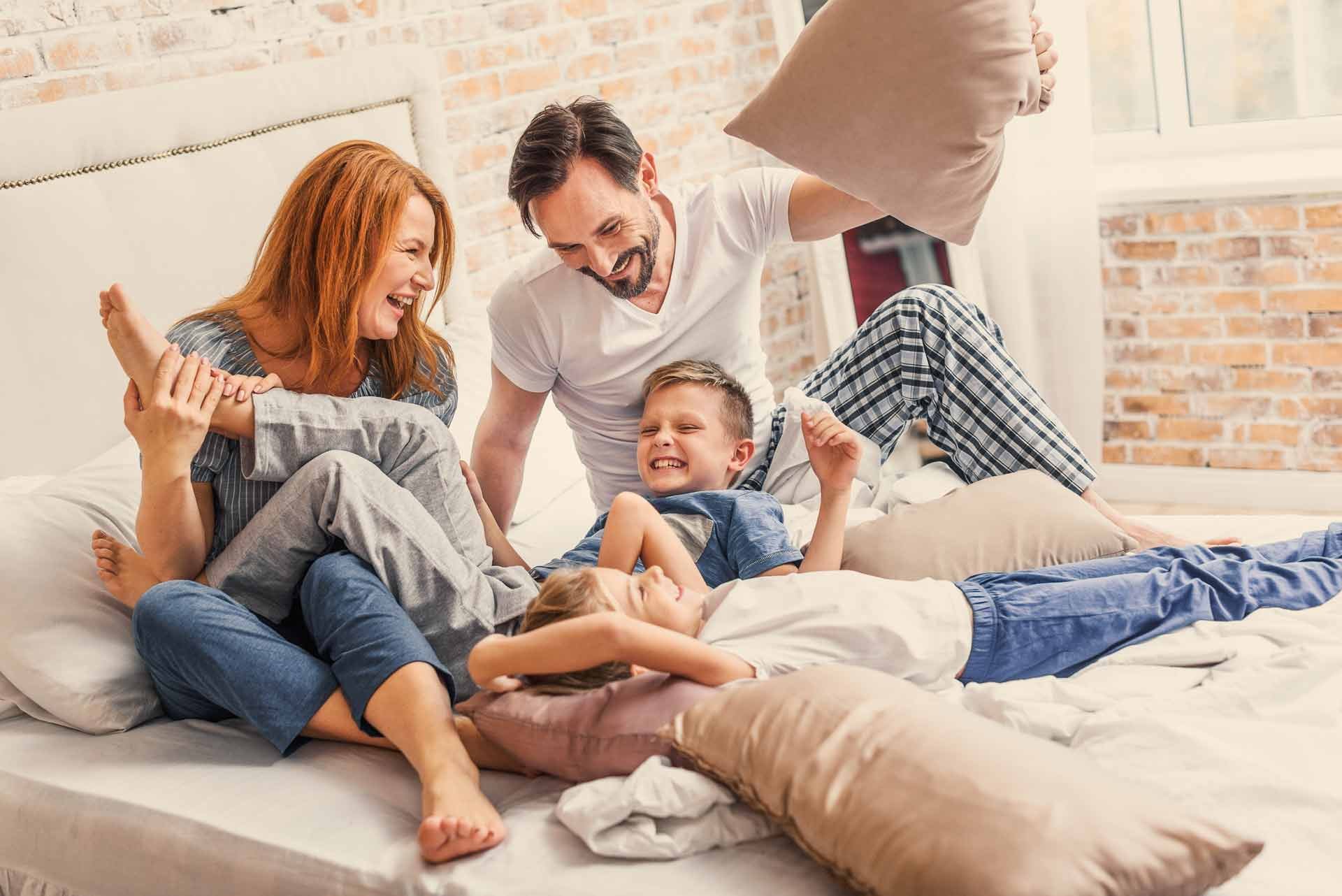 Parents and two sons having a pillow fight together on bed