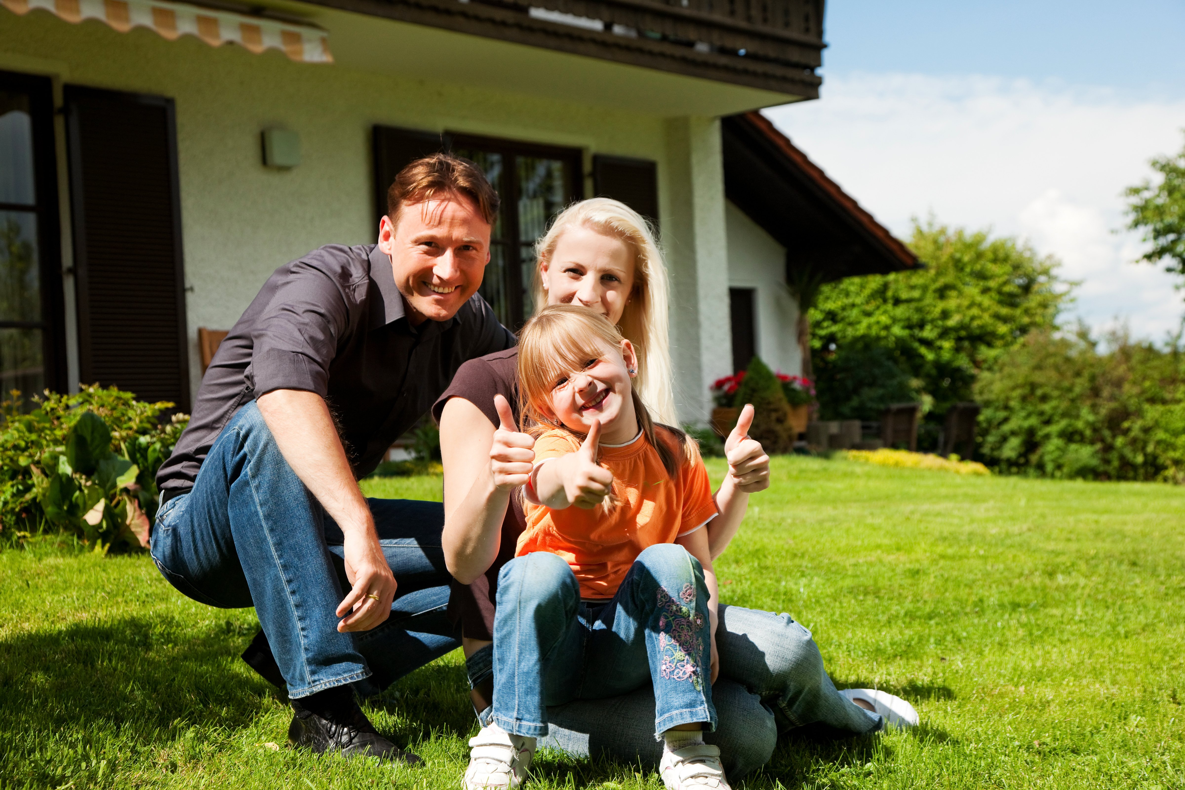 A family of three is pictured on the lawn outside their home in a rural area.