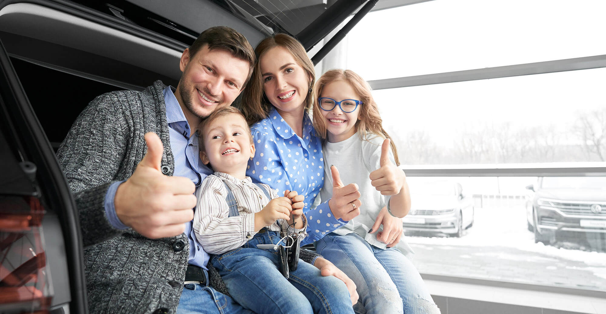 A happy family is sitting in the trunk of their car after an auto loan refinance.