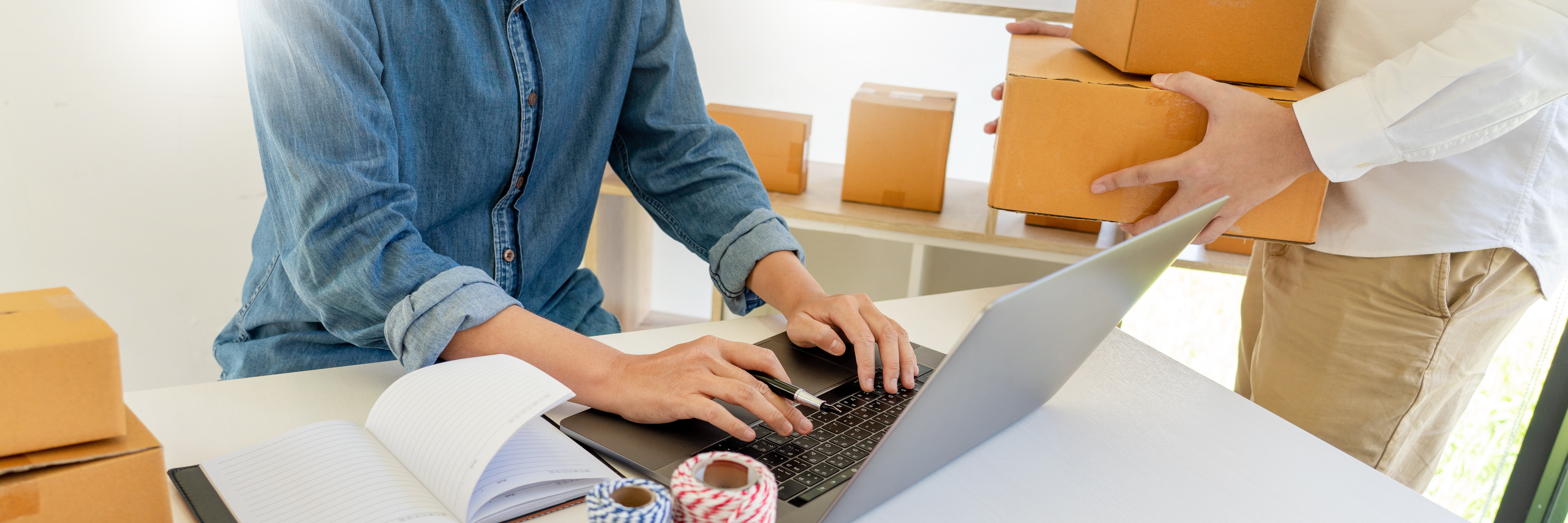 A small business owner works with an employee to pack and ship online orders.