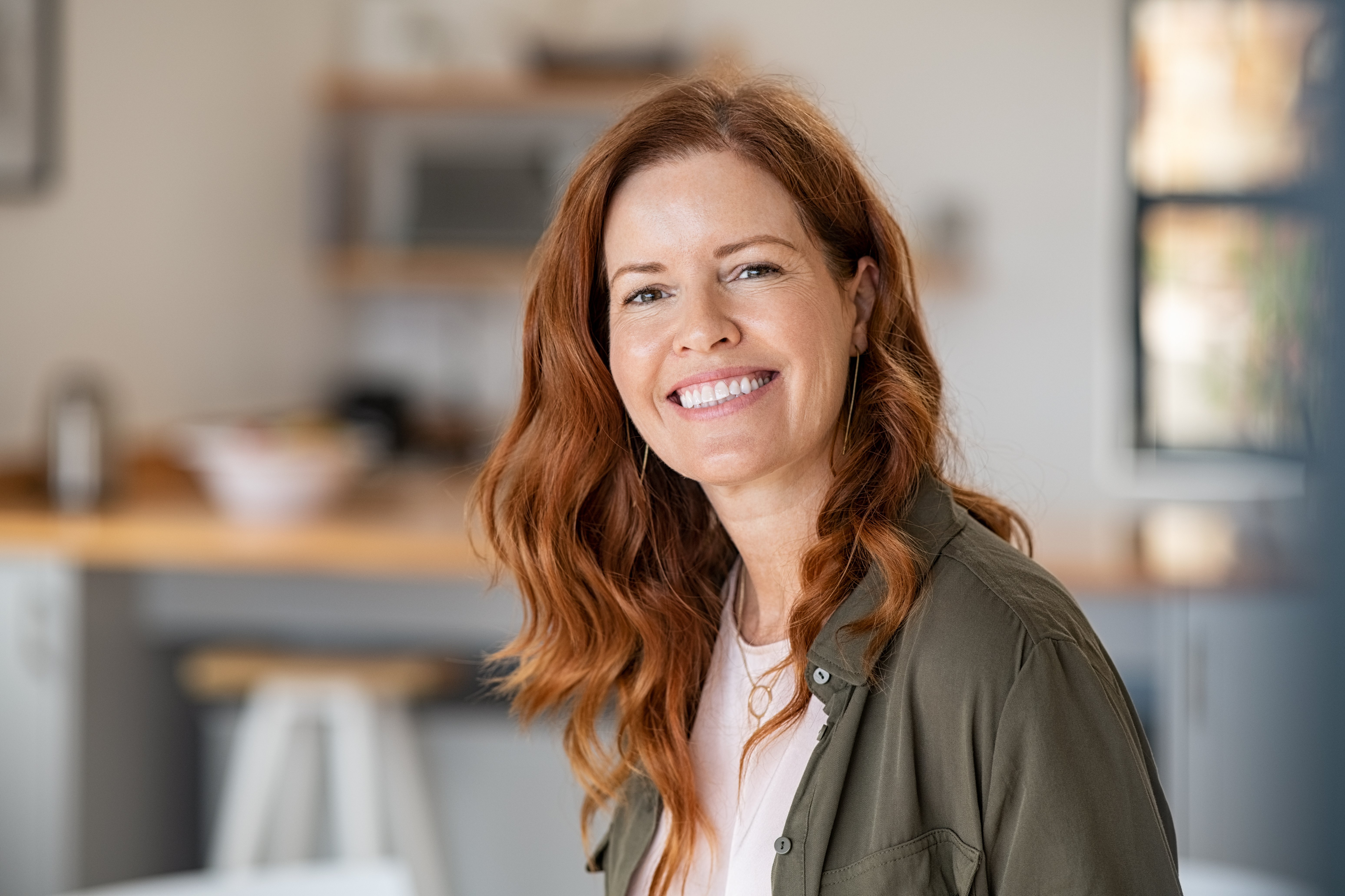 A woman smiles as she sits in her kitchen, knowing she has made a wise choice by investing in a Traditional IRA.