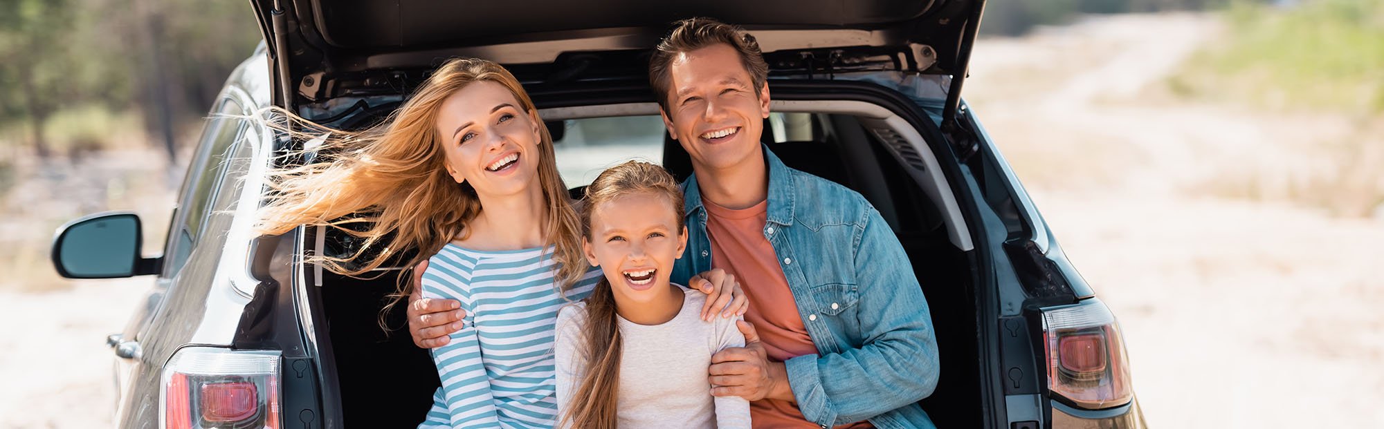 A happy family is sitting in the trunk of their car with an auto loan.