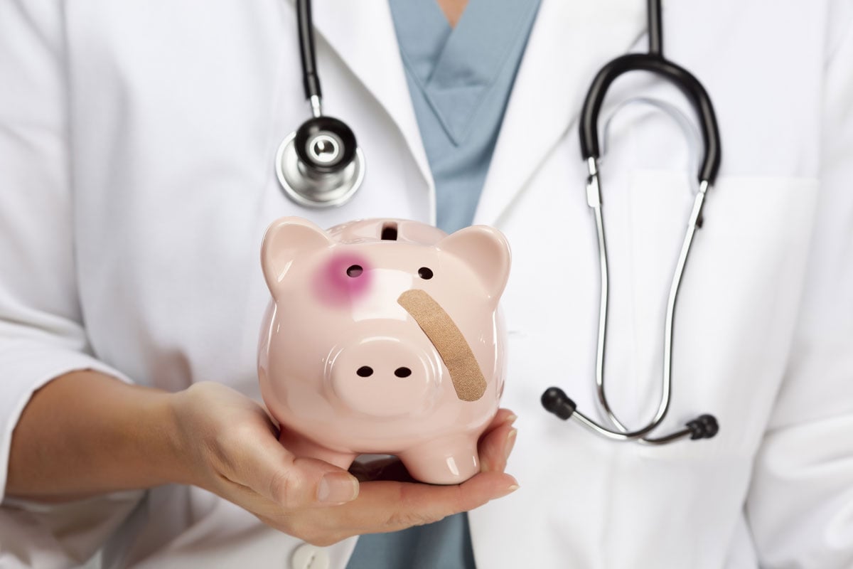 Piggy bank with black eye and bandaid held in a doctor's hand