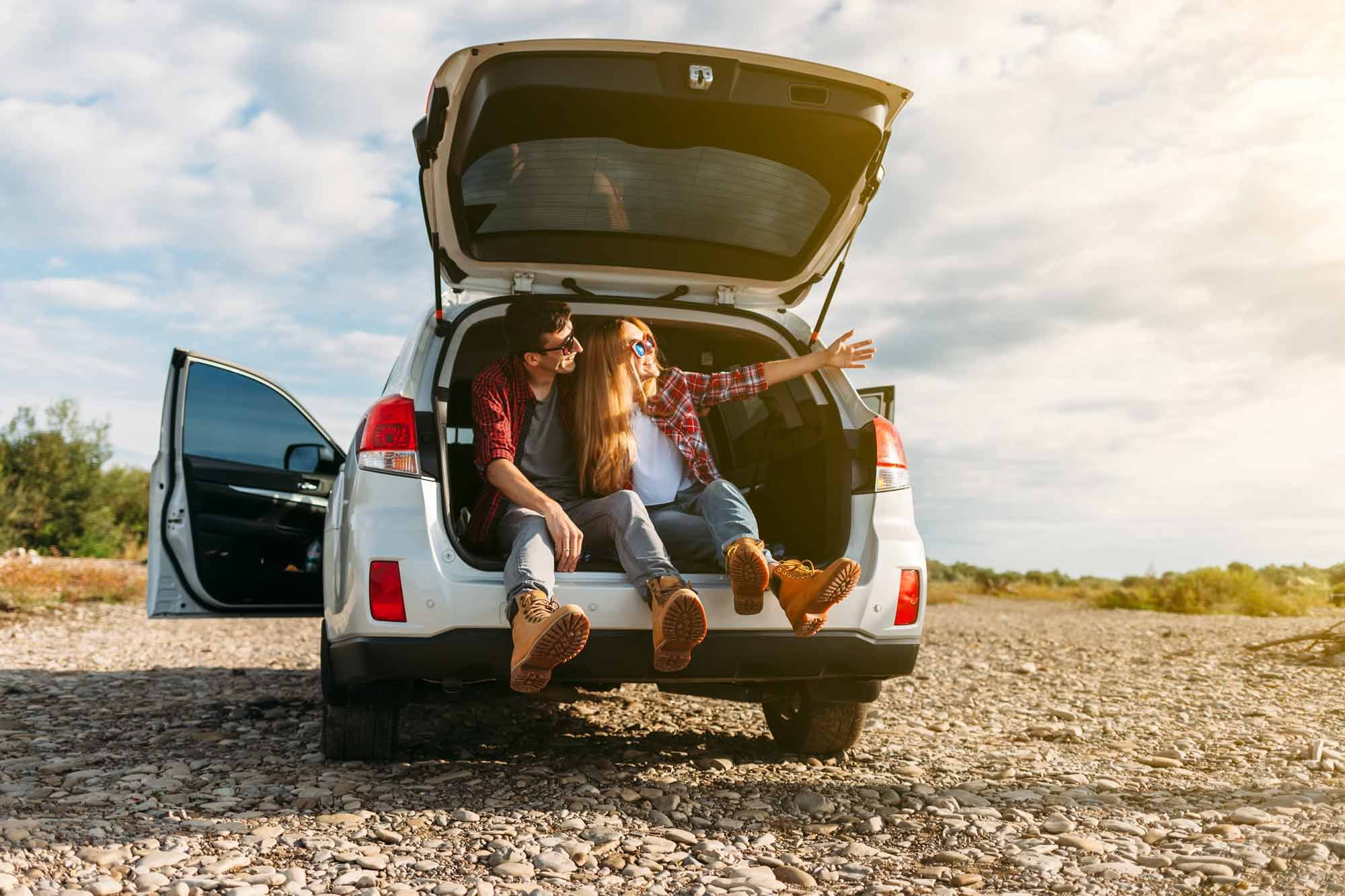 Couple sitting in open back of car with open hatch on rocky road