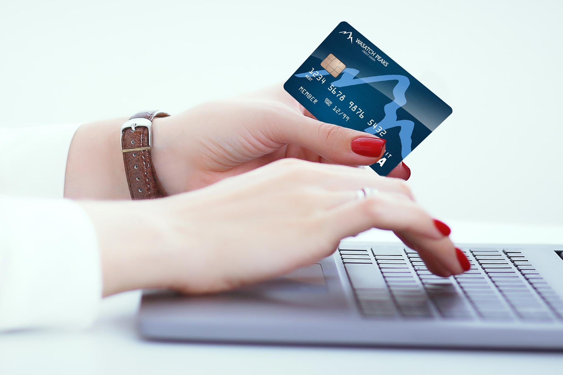 Woman's hands typing on laptop while holding a Wasatch Peaks debit card