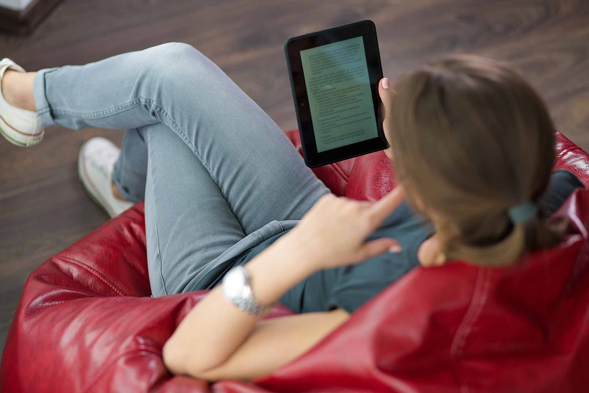 Woman sitting on bean bag reading eBook on tablet device