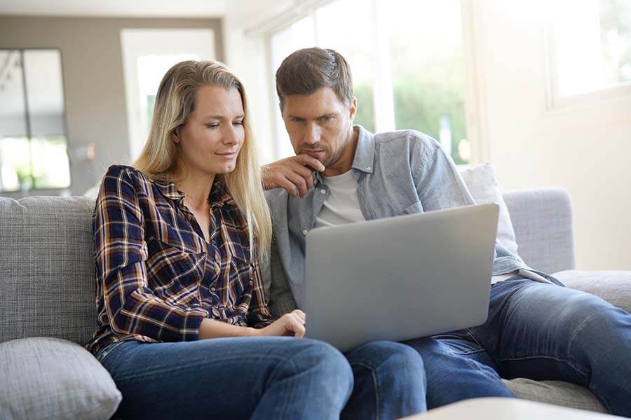 A couple at home researching money market account pros and cons on their laptop.
