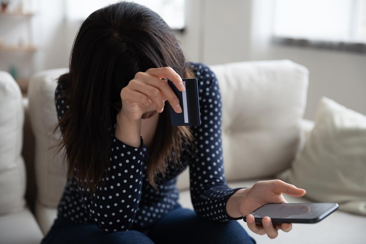 Upset woman holding credit card and phone after a shopping scam