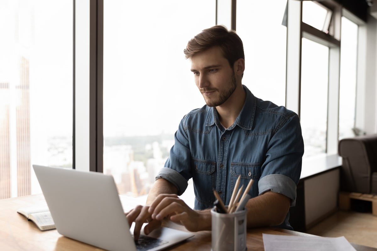 A pensive younger man does research on his laptop to see if you can add to a money market account regularly.