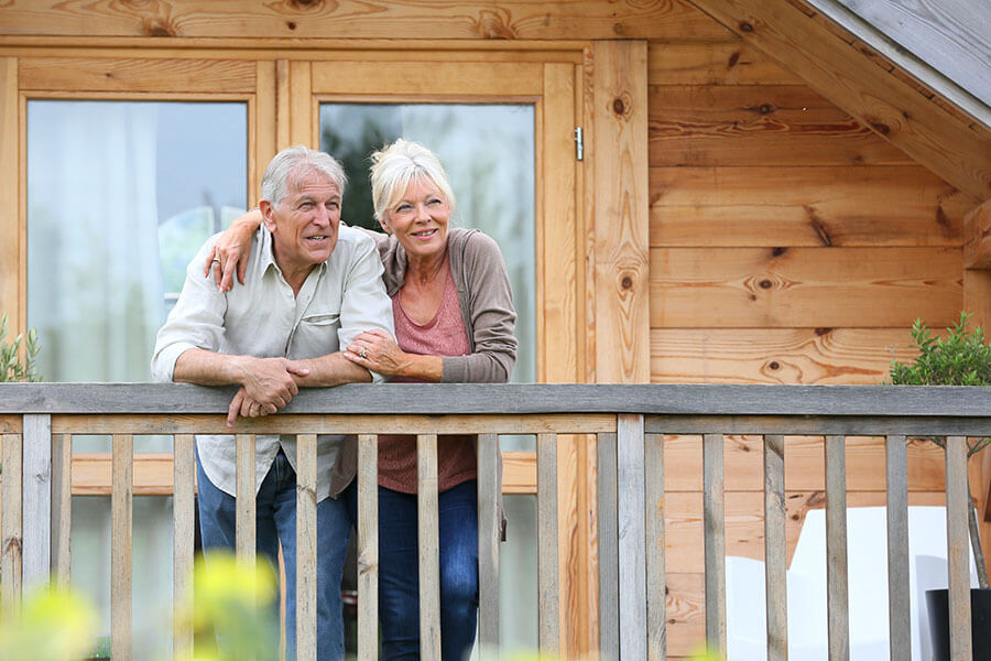 An older couple standing on the deck of a cabin they bought using home equity to purchase a new home.