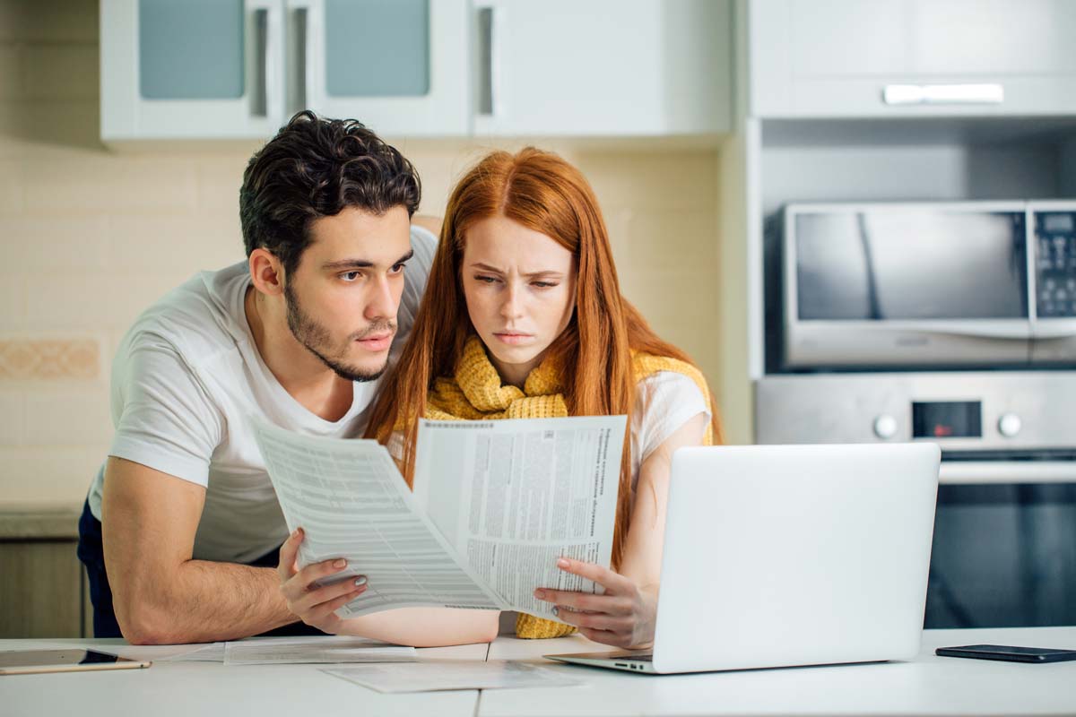 Couple looking focused at papers and at laptop in kitchen