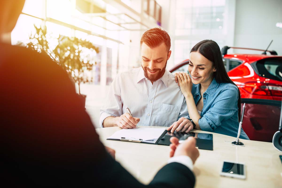 couple signing paperwork at car dealership