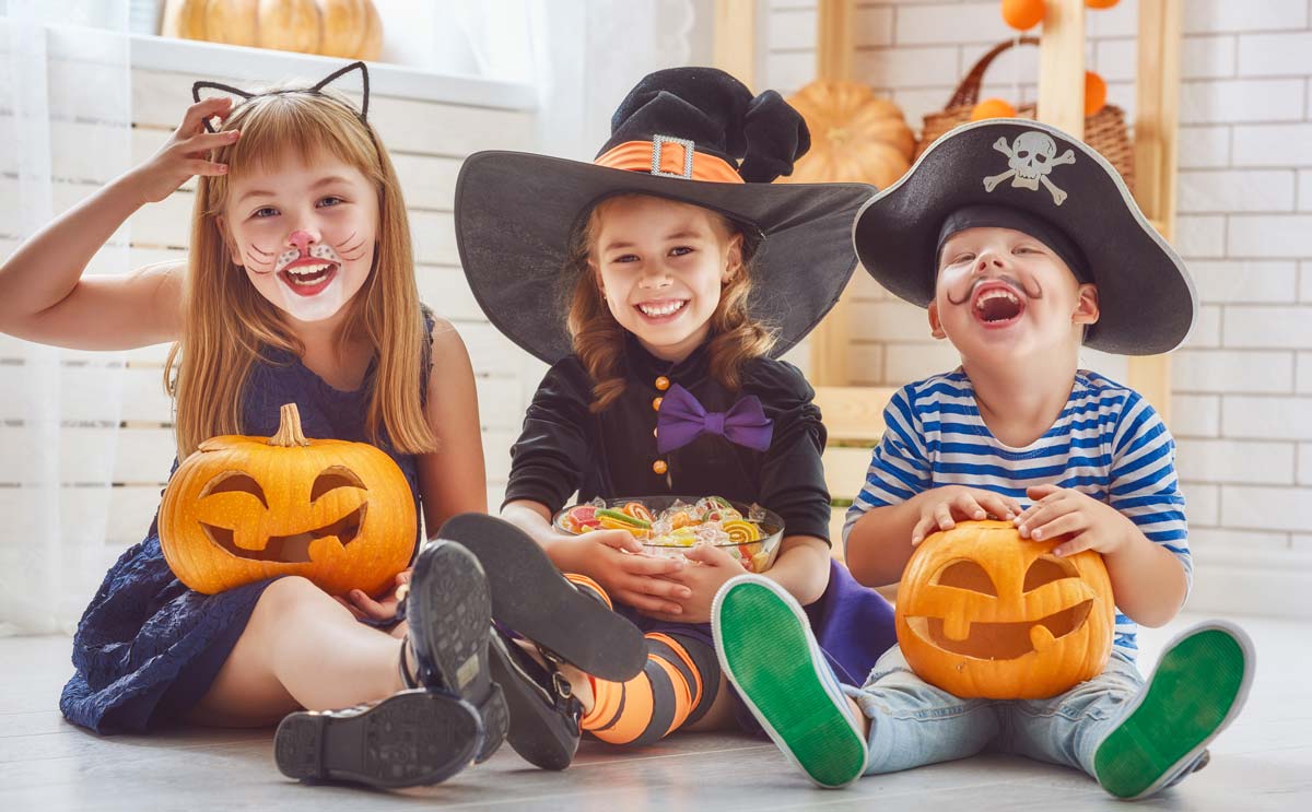 kids in costumes laughing together with pumpkins and candy