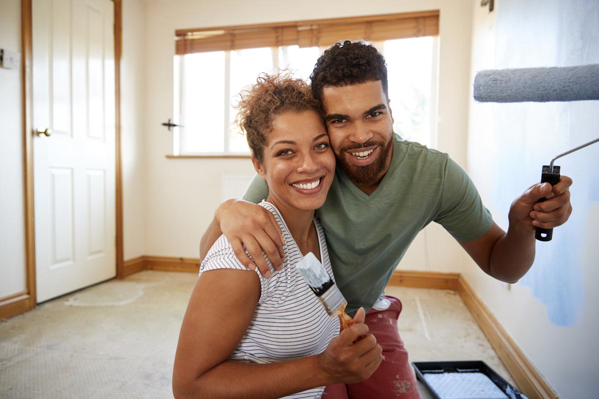 Couple smiling and holding paint brush and roller