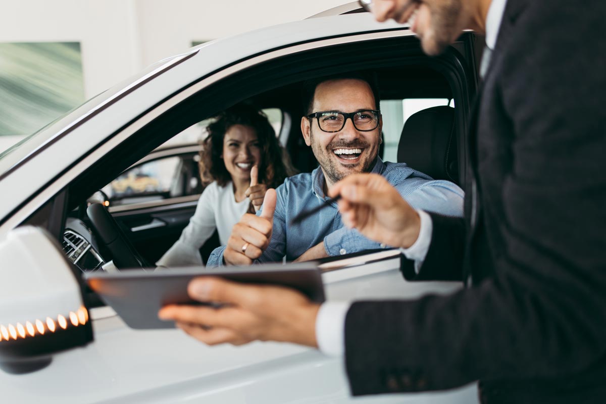 Man and woman inside car talking to salesman