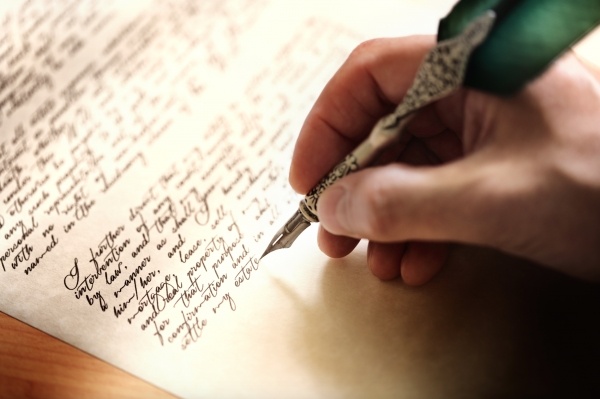 hand with pen writing in cursive on paper