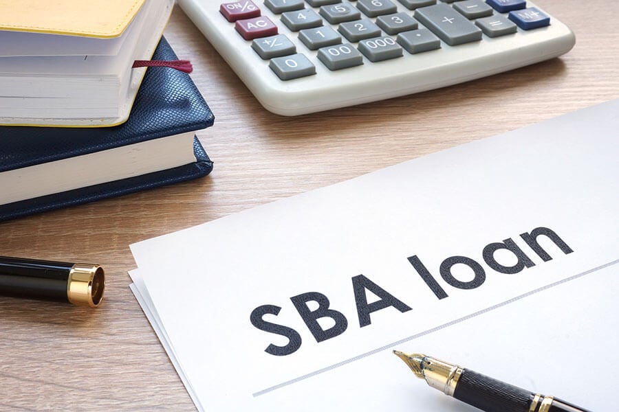 SBA loan paperwork on a desk with a pen, calculator, and stack of books