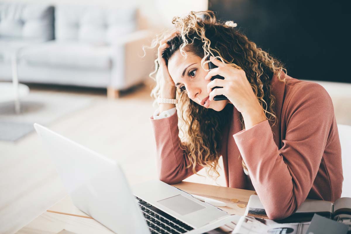 Upset woman talking on phone while looking at her laptop and recovering from identity theft