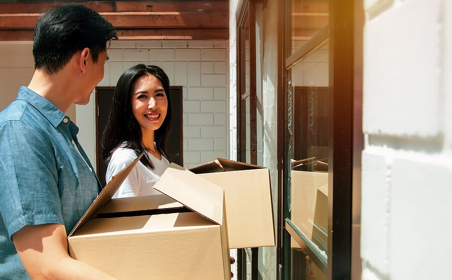 A young Asian couple carrying boxes stand at the entrance of their new home