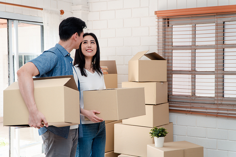 A smiling couple holding moving boxes walk into their new home. Learn about the main steps in the mortgage process.