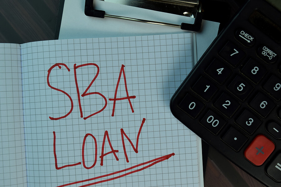 SBA loan written in big red letters on graph paper next to a calculator and clipboard