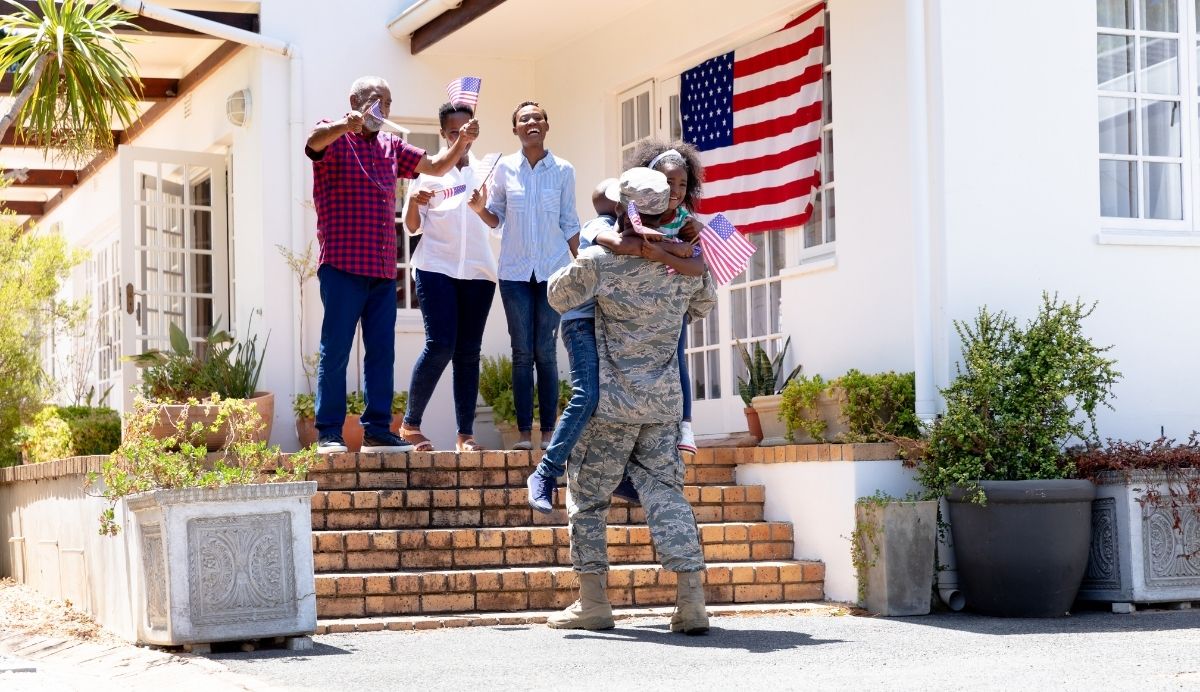 a military family stands outside of their house with American flags happy to welcome home an active-duty loved one