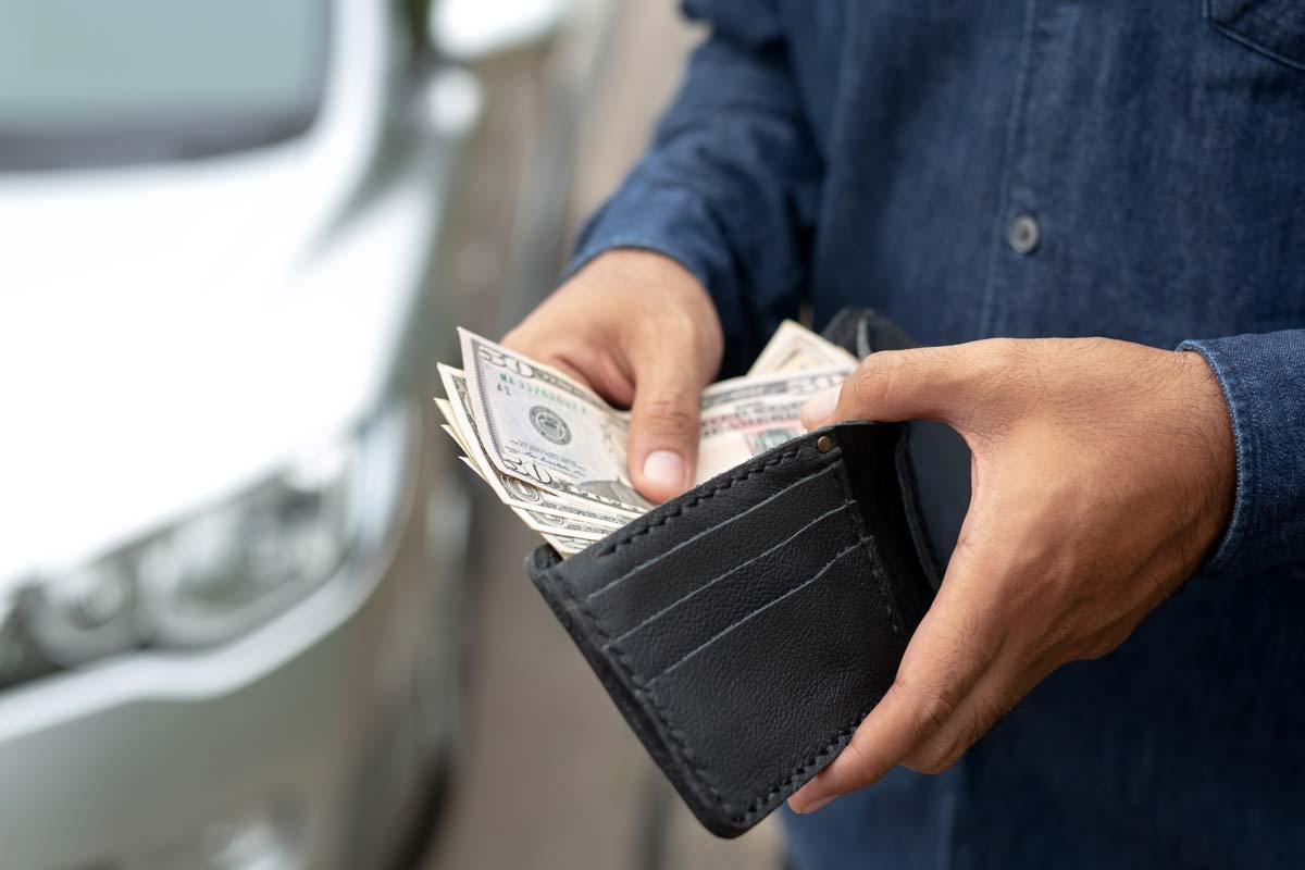 hand holding wallet with money, car behind them