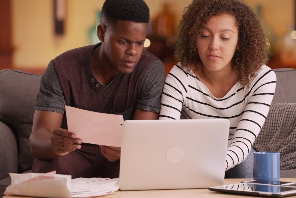 A young African American couple reviews HELOC debt consolidation on their laptop.