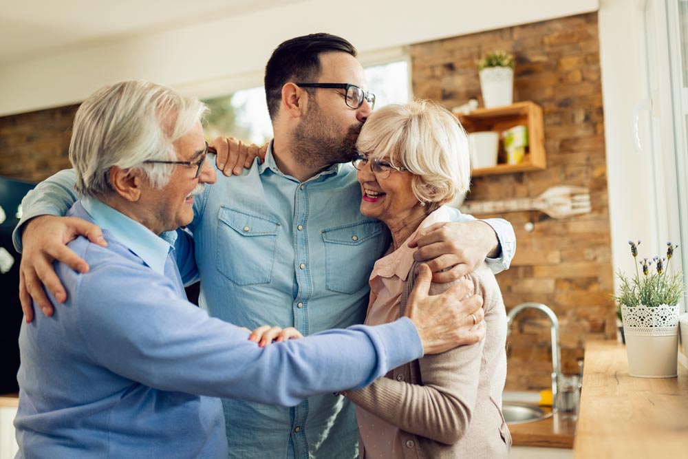 Adult son hugging parents in kitchen